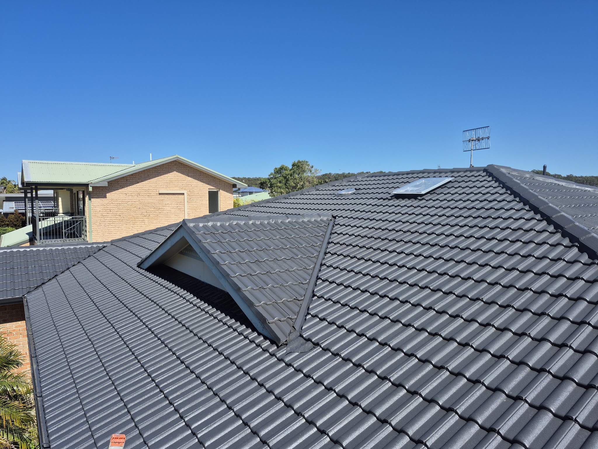 Close view of a finished charcoal tile roof against a clear blue sky