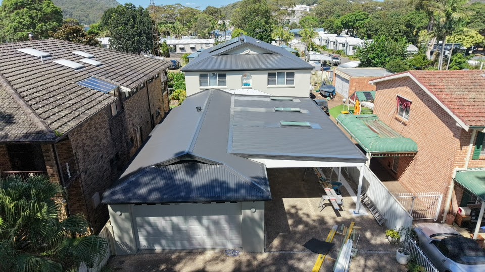 Aerial view of a finished grey metal roof and carport with bush hills behind