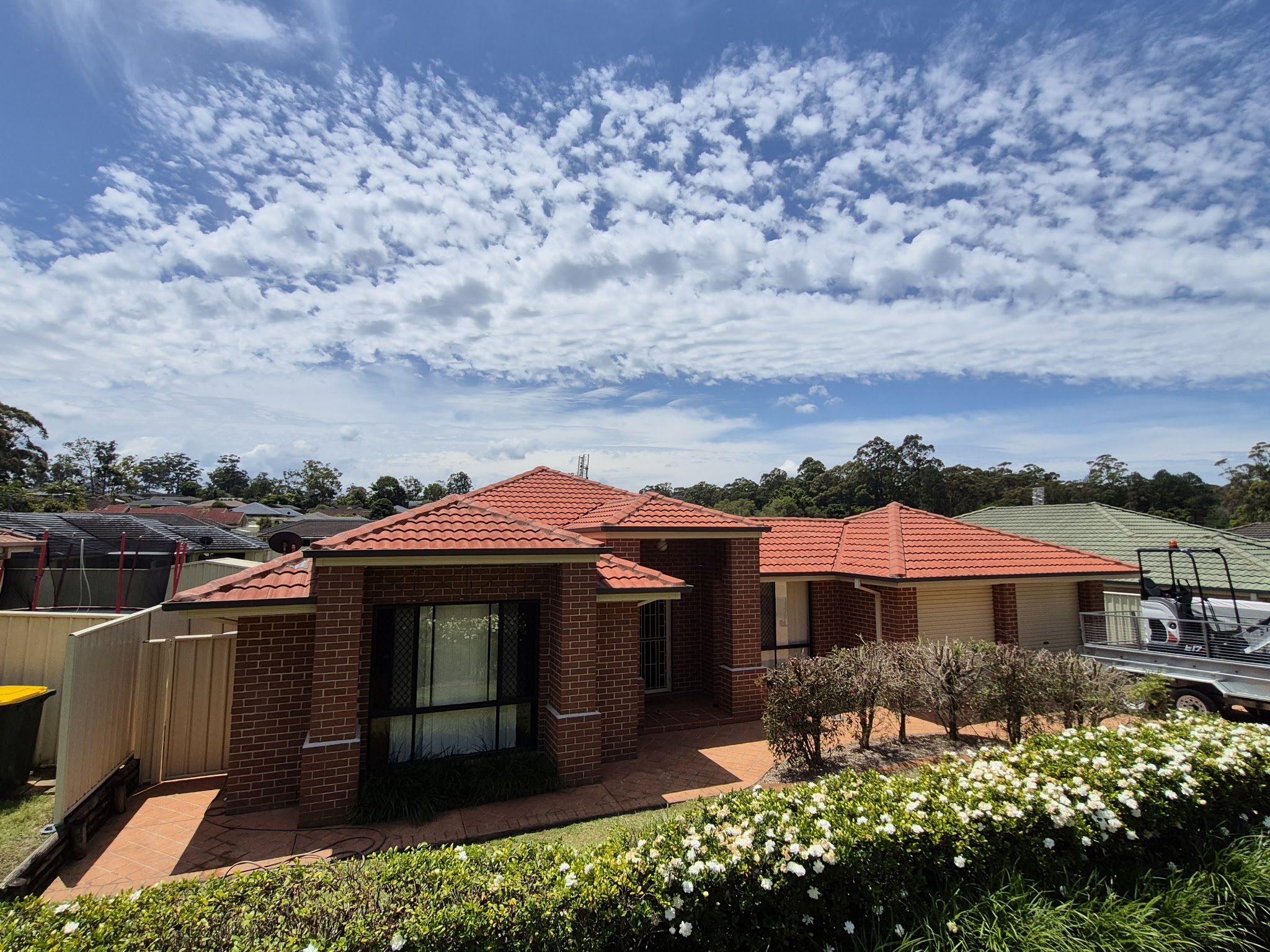 Restored terracotta tile roof on a brick home under a cloud streaked sky