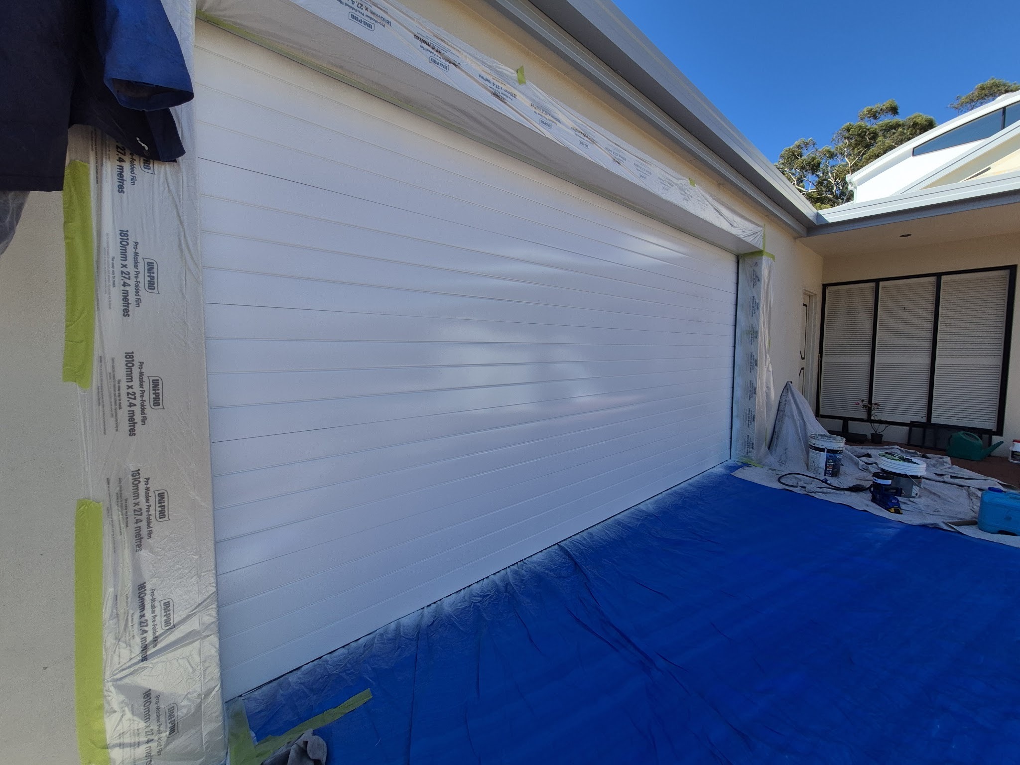 A garage door and wall masked off with drop sheets and plastic film before spraying